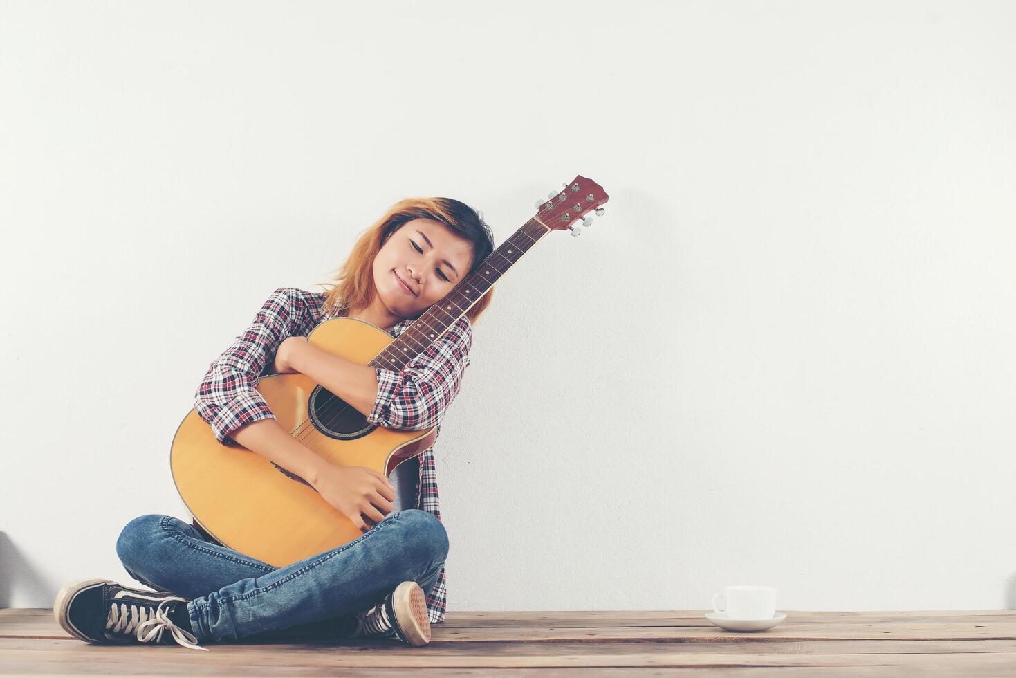 vacker kvinna sitter med sin gitarr lyckligt sitter på trä foto