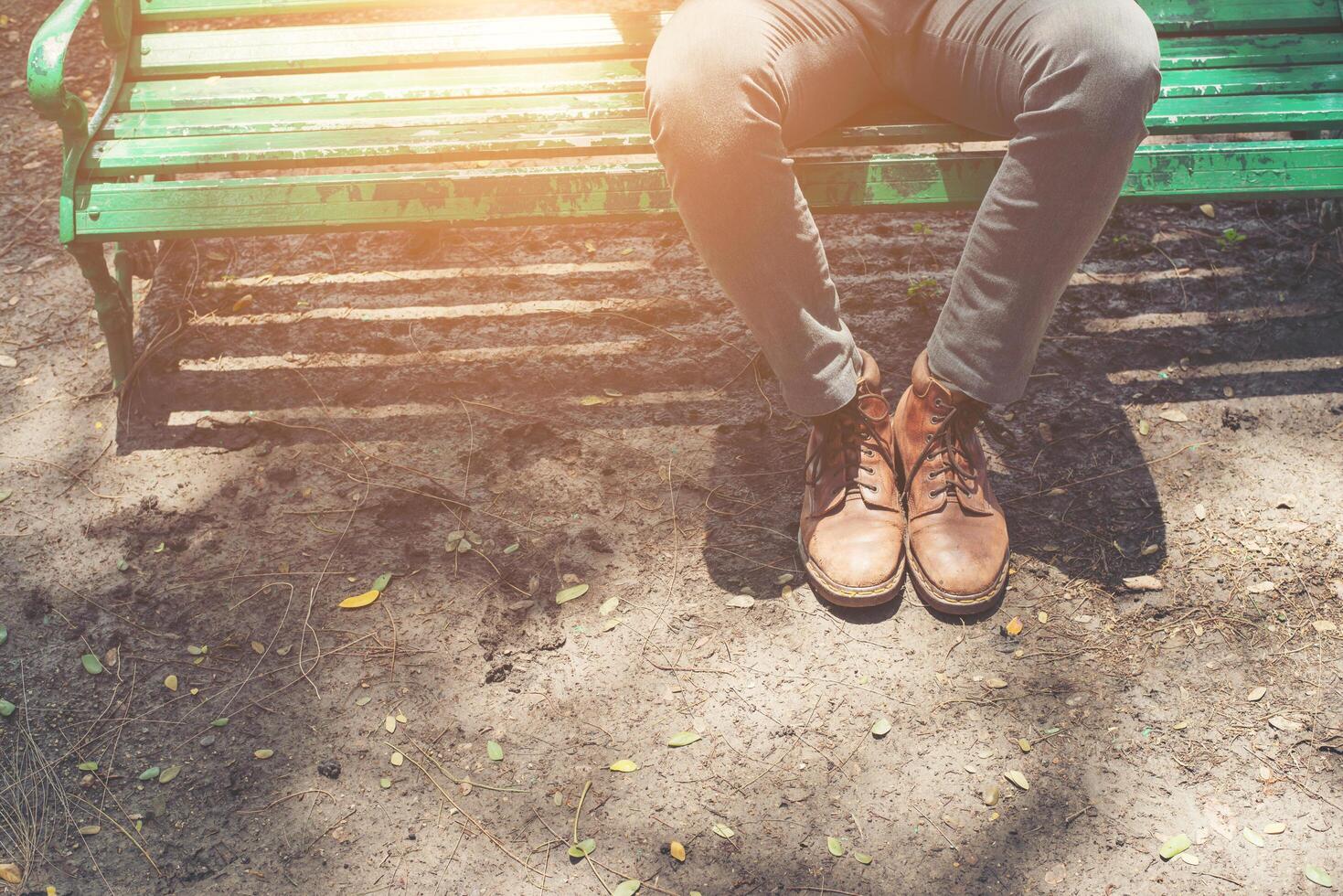 hipster kille sitter på bänken med jeans och bruna sämskskor. foto