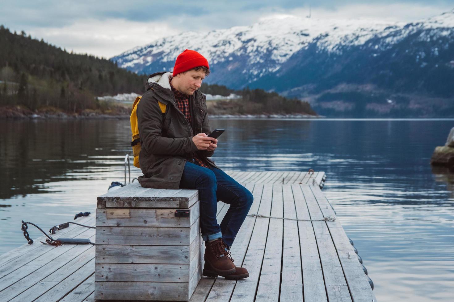 resenär man tittar in i telefonen sitter på träbrygga foto