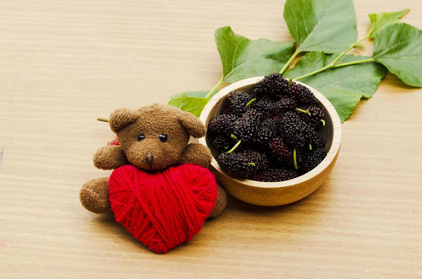 närbild av teddy dol med rött hjärta och mullbärsfrukter foto