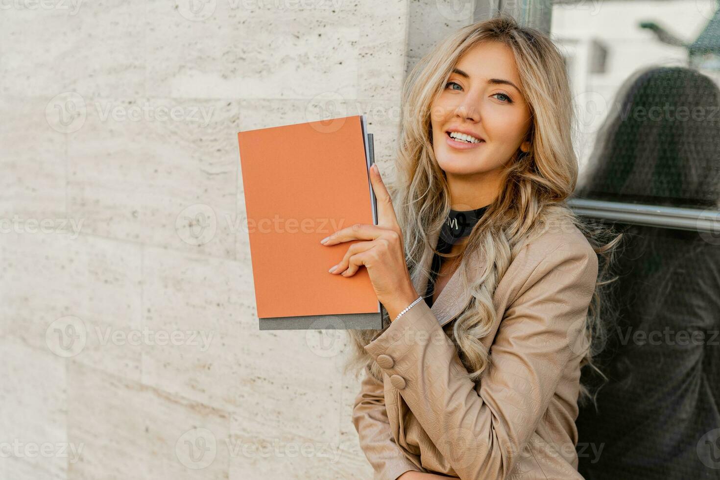 stänga upp Foto av elegant framgångsrik blond kvinna i eleganta tillfällig utrusta Framställ på de gata. innehav reklam kataloger.