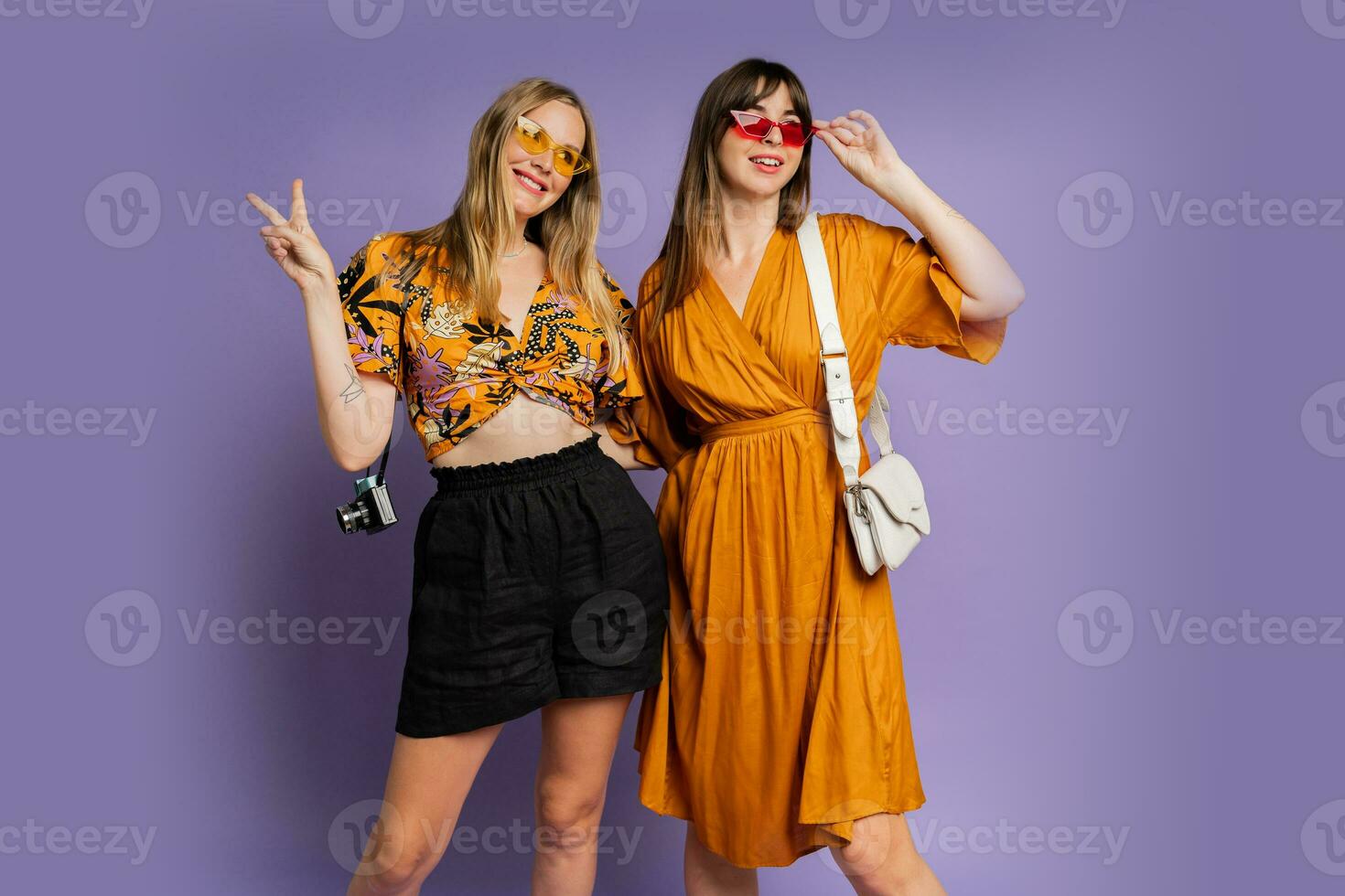 två Söt kvinnor , bäst vänner, Framställ på lila bakgrund i trendig sommar utrusta. foto