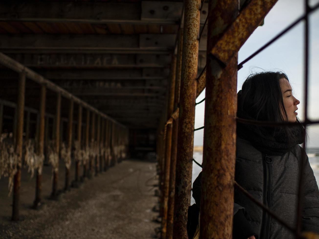 ung flicka i kappa står nära metallrostiga strukturer foto