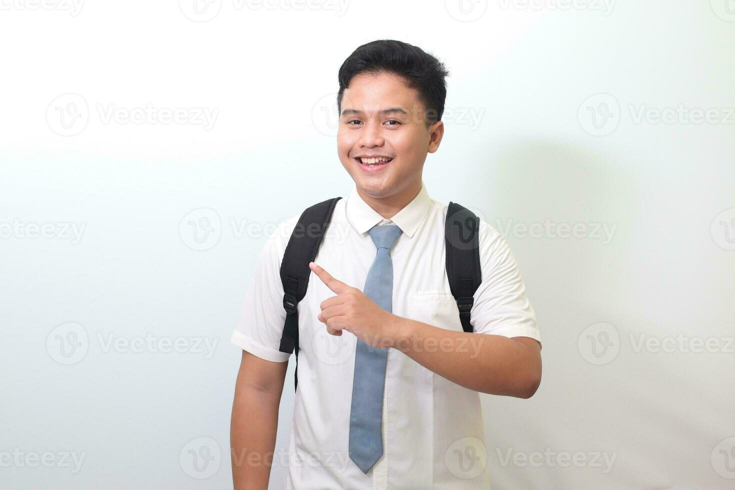 indonesiska senior hög skola studerande bär vit skjorta enhetlig med grå slips som visar produkt, pekande på något och leende. isolerat bild på vit bakgrund foto