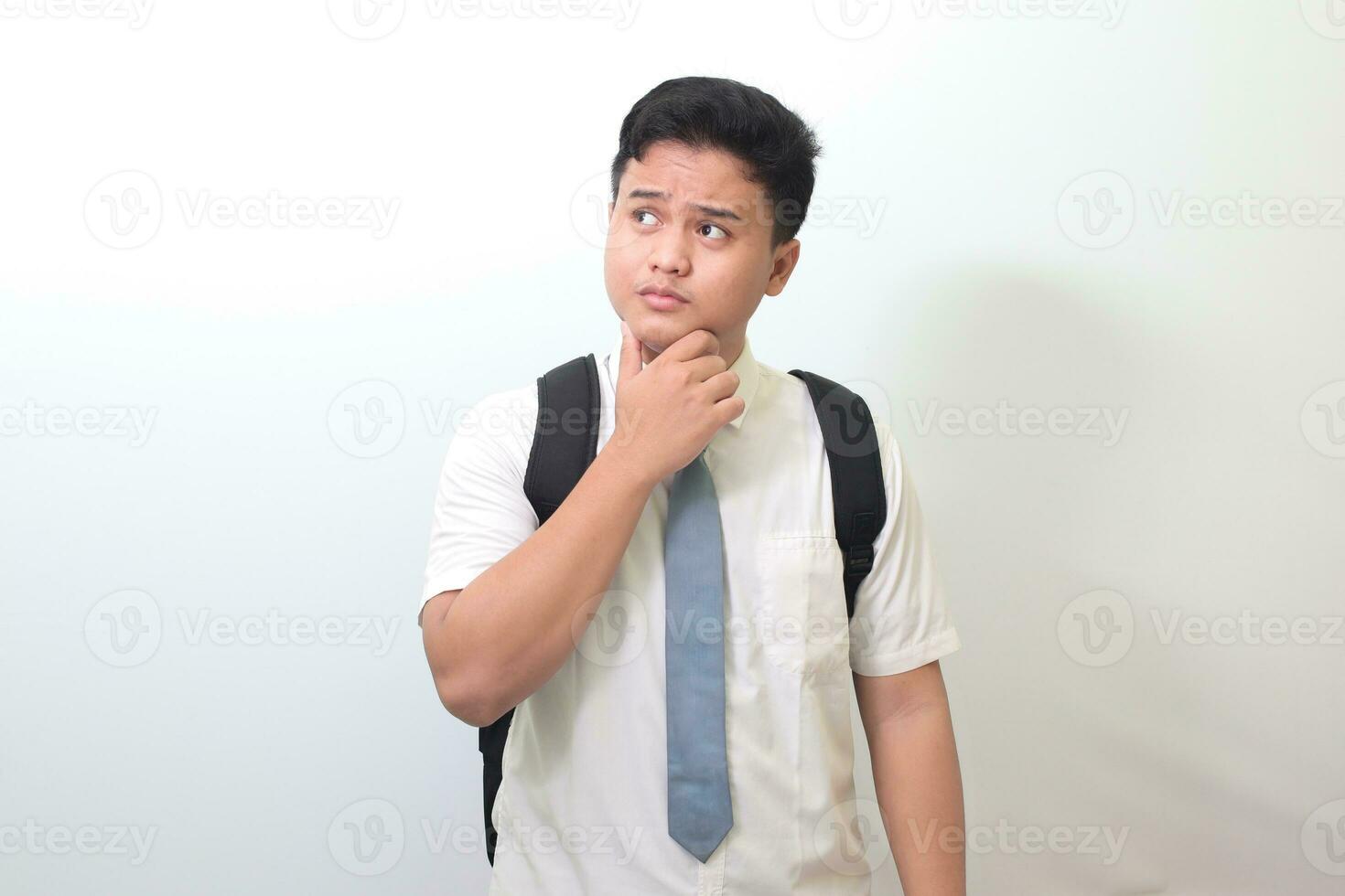 indonesiska senior hög skola studerande bär vit skjorta enhetlig med grå slips och tänkande handla om fråga med hand på haka. isolerat bild på vit bakgrund foto