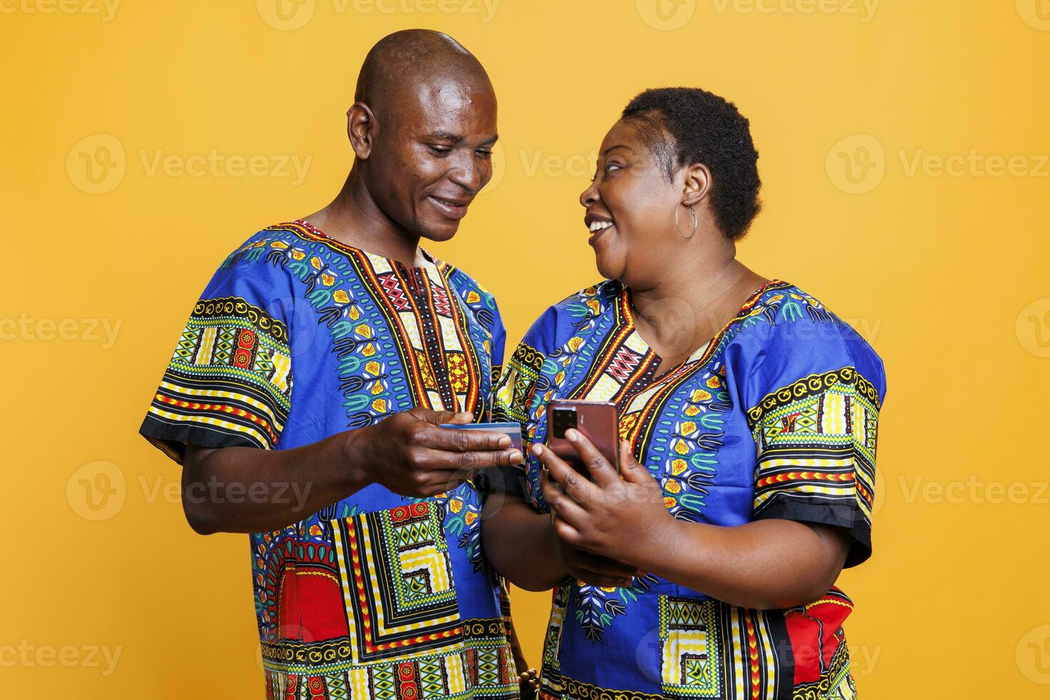 glad man och kvinna par bearbetning kolla upp uppkopplad använder sig av kreditera kort och smartphone app. leende svart fru och Make bär etnisk kläder njuter e-handel handla tillsammans foto