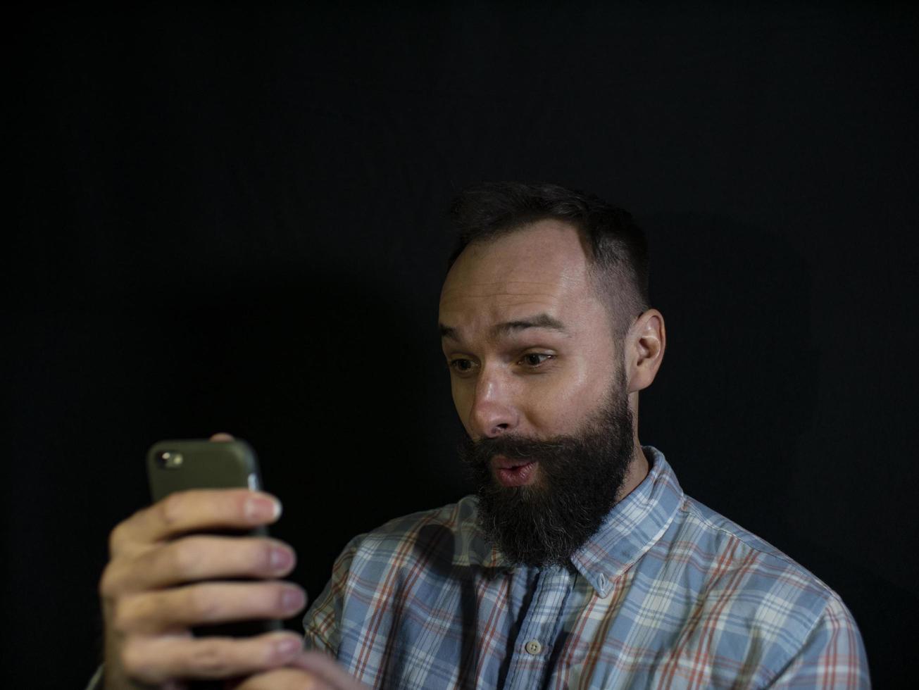 man med skägg och mustasch tittar in i en mobiltelefon foto