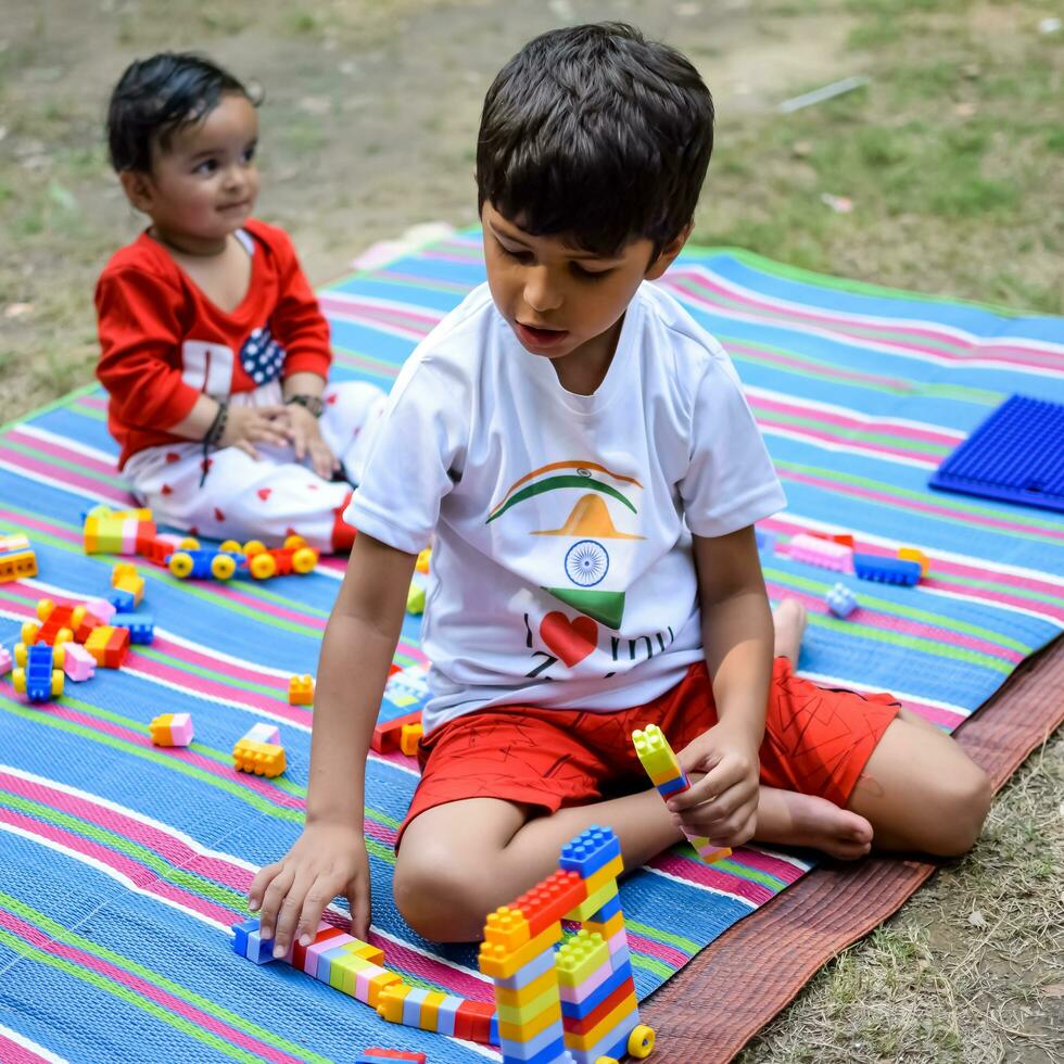 två Lycklig Pojkar i samhälle parkera, Lycklig asiatisk bröder vem är leende lyckligt tillsammans. bröder spela utomhus i sommar, bäst vänner. litet barn bebis pojke spelar med hans Lycklig bror i de trädgård foto