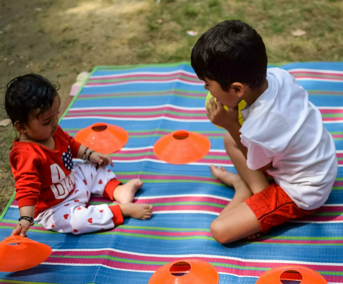 två Lycklig Pojkar i samhälle parkera, Lycklig asiatisk bröder vem är leende lyckligt tillsammans. bröder spela utomhus i sommar, bäst vänner. litet barn bebis pojke spelar med hans Lycklig bror i de trädgård foto