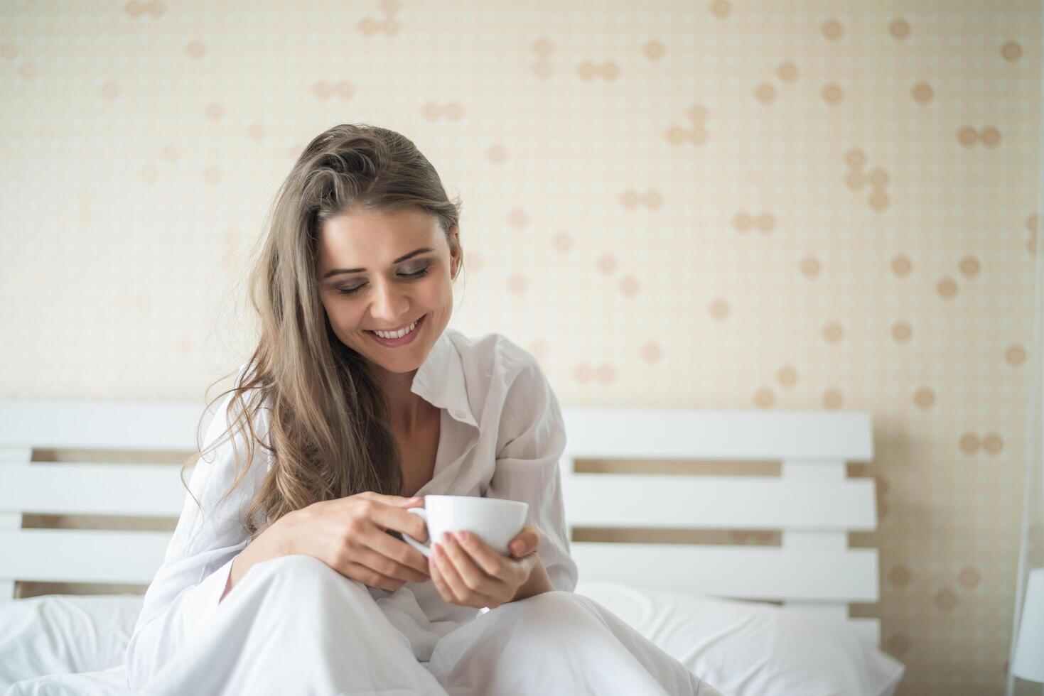 vacker kvinna i hennes sovrum som dricker kaffe på morgonen foto