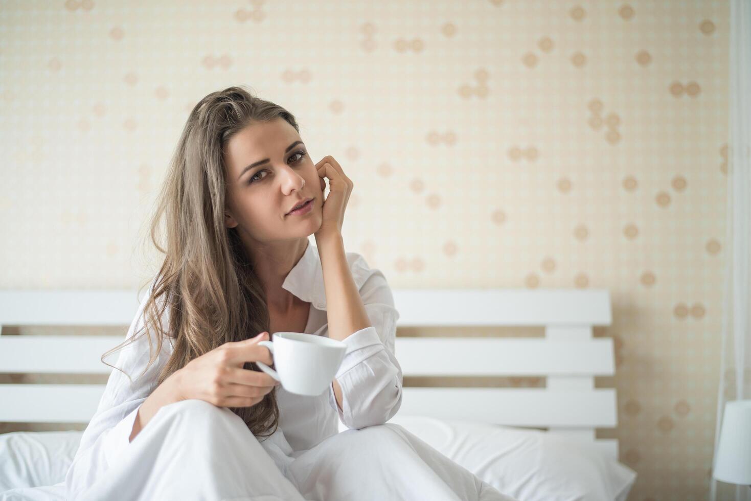 vacker kvinna i hennes sovrum som dricker kaffe på morgonen foto