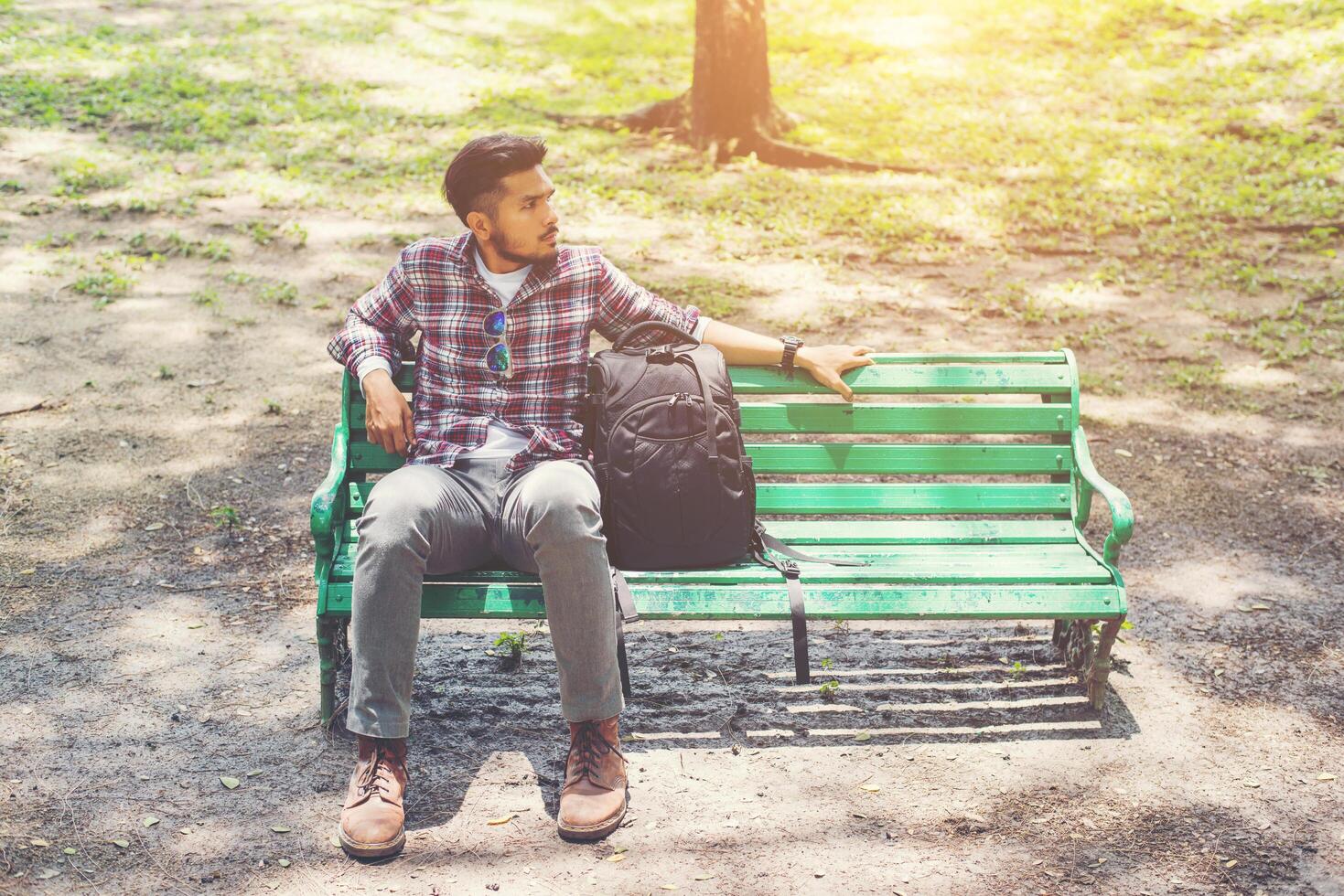 ung hipster man med ryggsäck bredvid sitter på en träbänk. foto