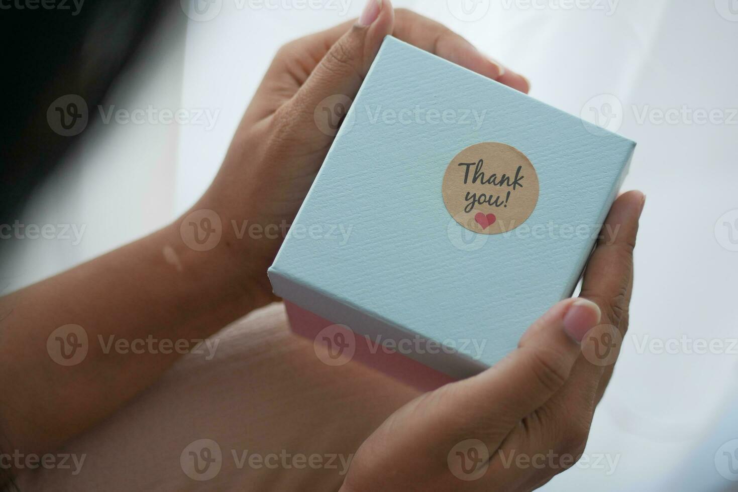 kvinnor hand sätta en tacka du klistermärke på en gåva låda foto