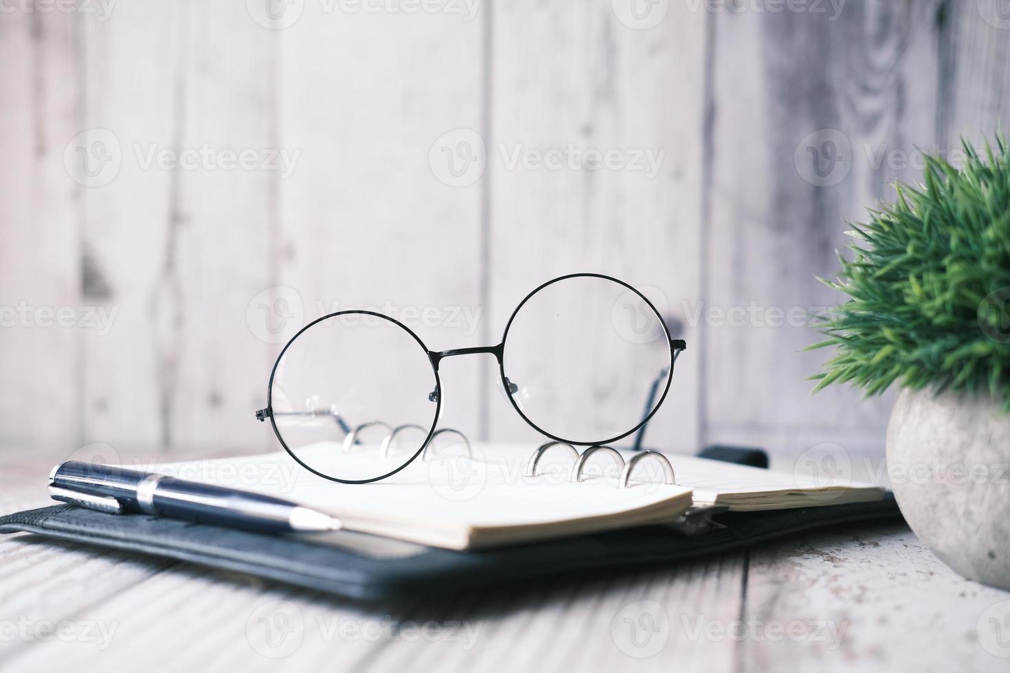 anteckningsblock, glasögon och en penna på träbord foto