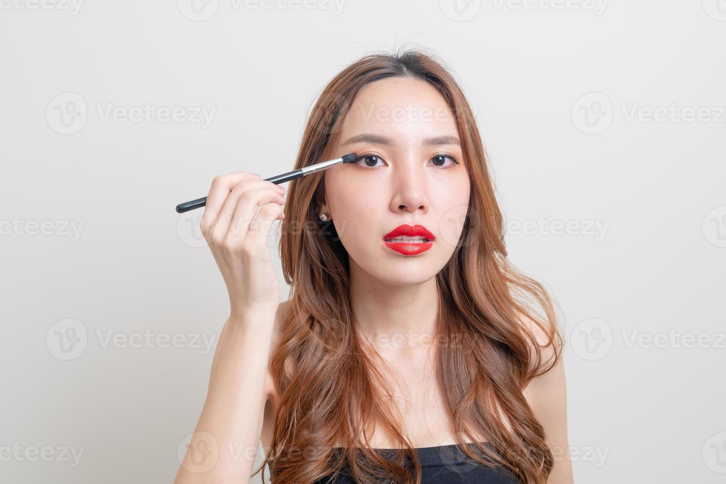 porträtt vacker asiatisk kvinna med sminkögonborste på vit bakgrund foto