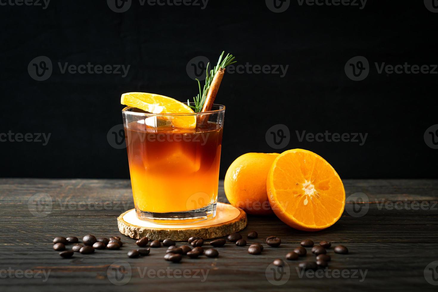 ett glas iced americano svart kaffe och lager av apelsin- och citronsaft dekorerad med rosmarin och kanel foto