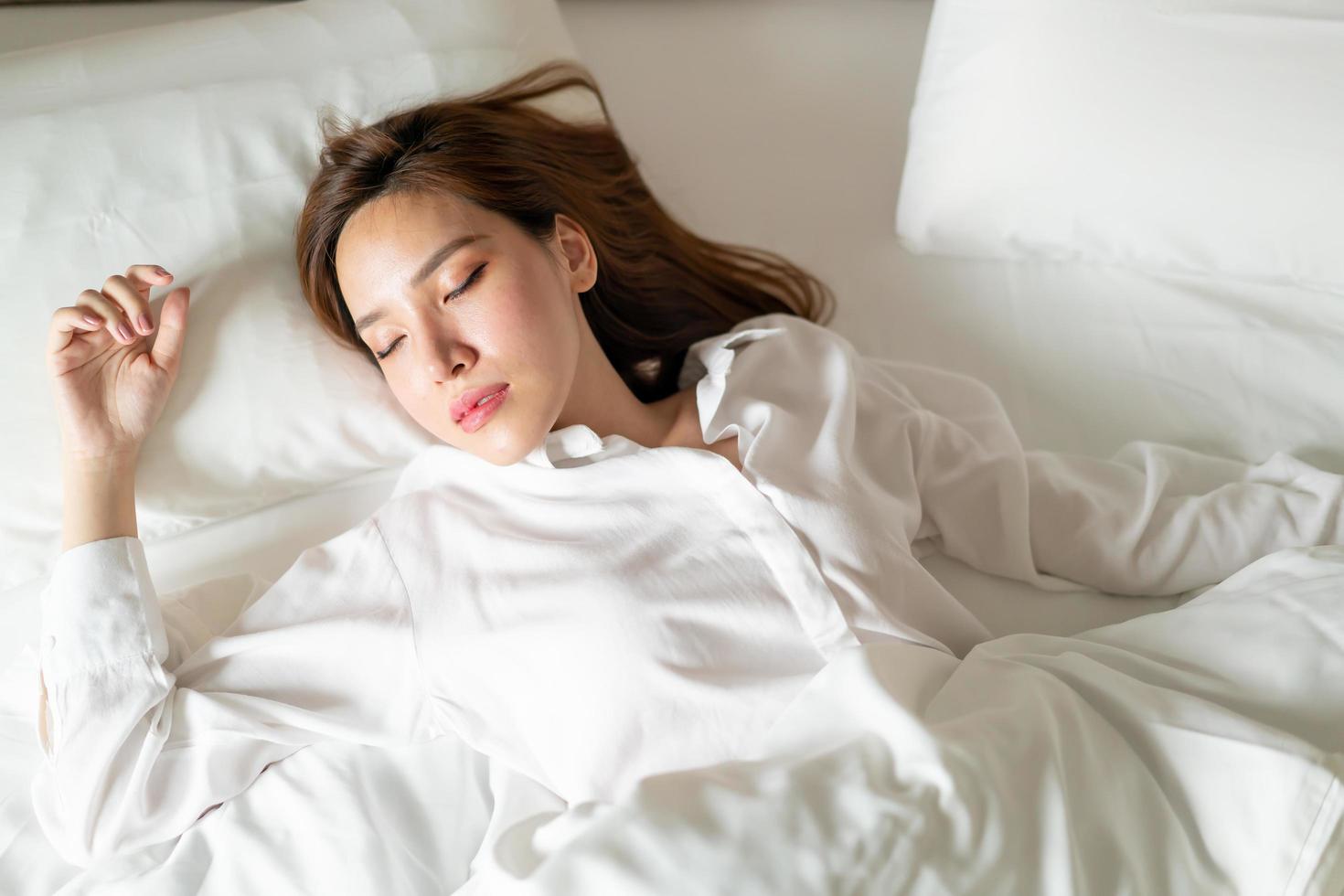 porträtt vacker asiatisk kvinna som sover på sängen med vit kudde foto