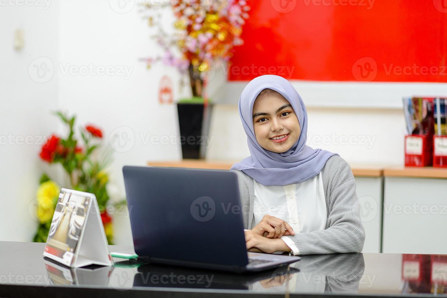 porträtt av asiatisk kvinna som sitter leende framför bärbar dator foto