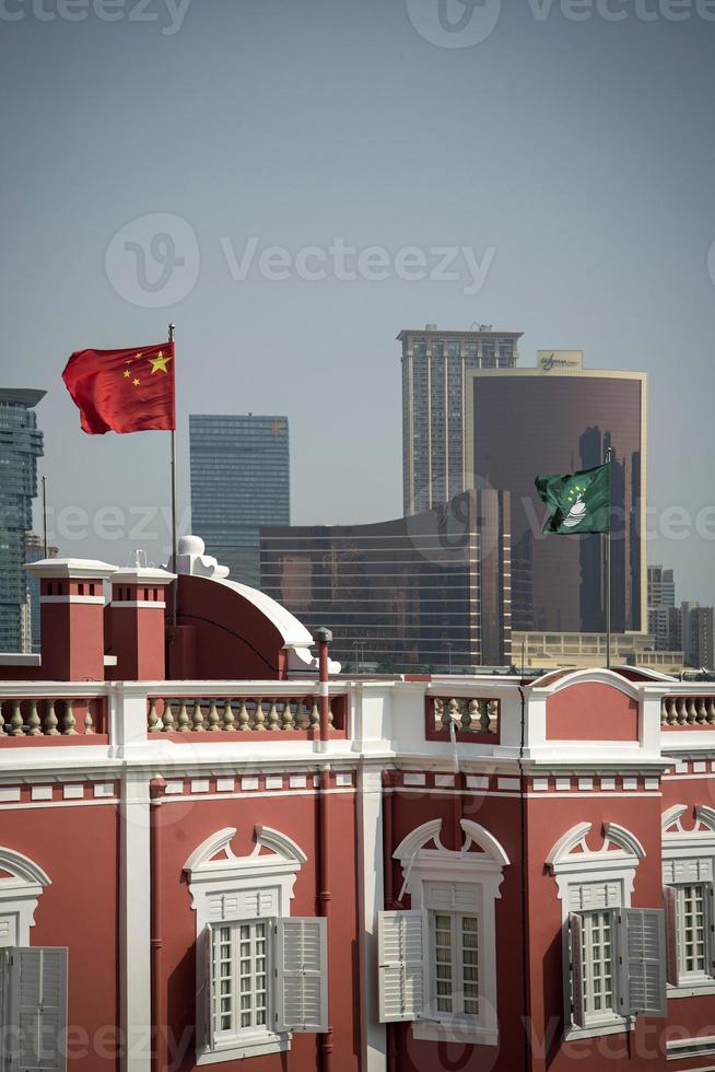 Kina och macau flaggor på den kinesiska regeringens huvudkontor i centrala macau city foto