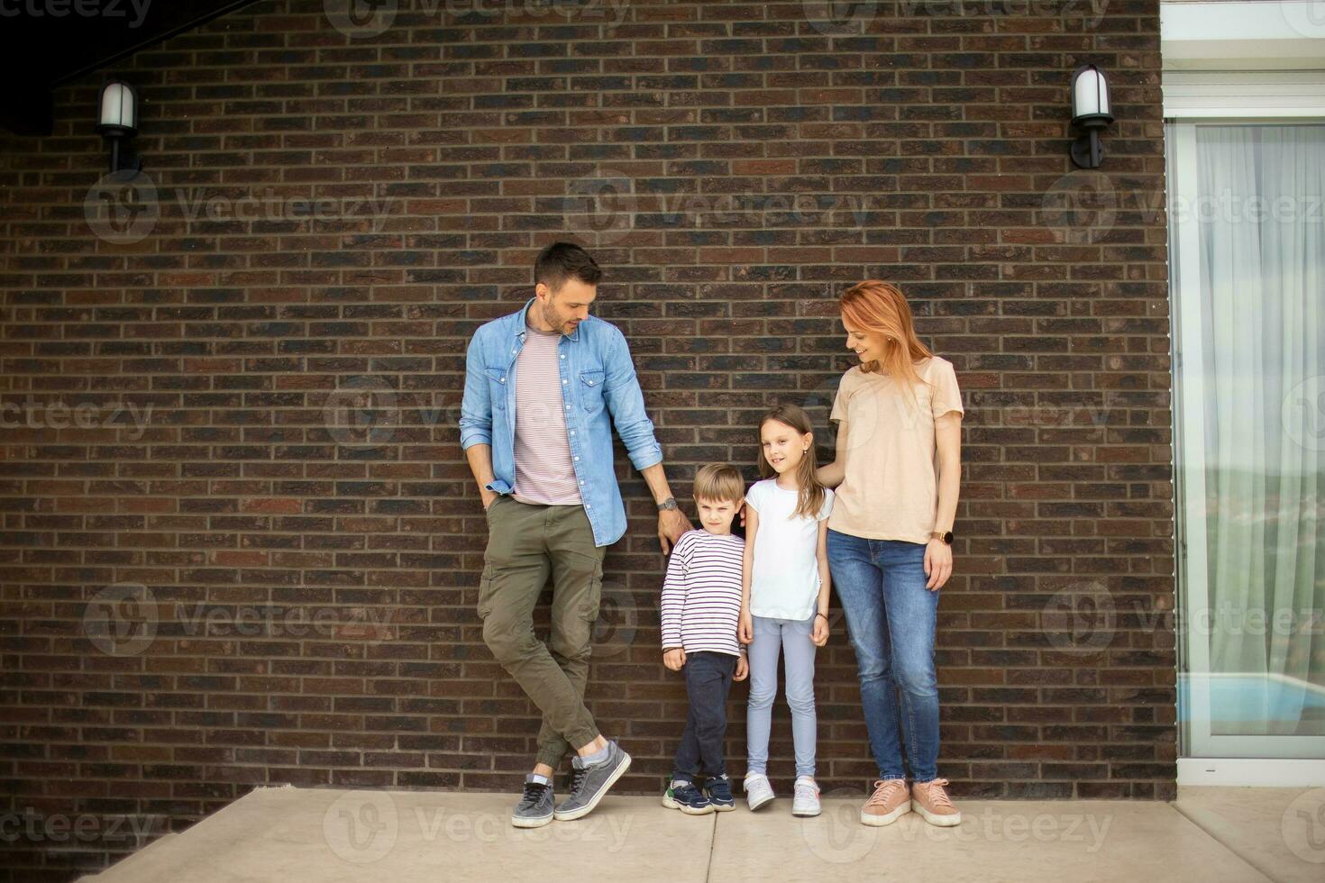 familj med en mor, far, son och dotter stående förbi de vägg av tegel hus foto