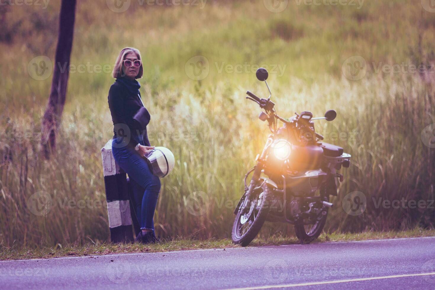 Söt kvinna innehav säkerhet hjälm stående på lokal- väg bredvid små enduro motorcykel foto