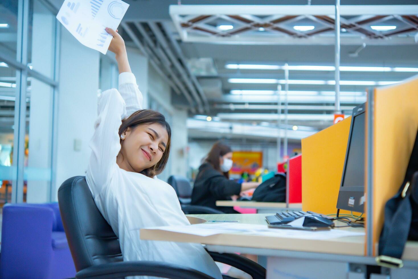 ung asiatisk företag kvinna sitter ner efter utmattning från en lång dag av pappersarbete i henne kontor, digital marknadsföring. foto