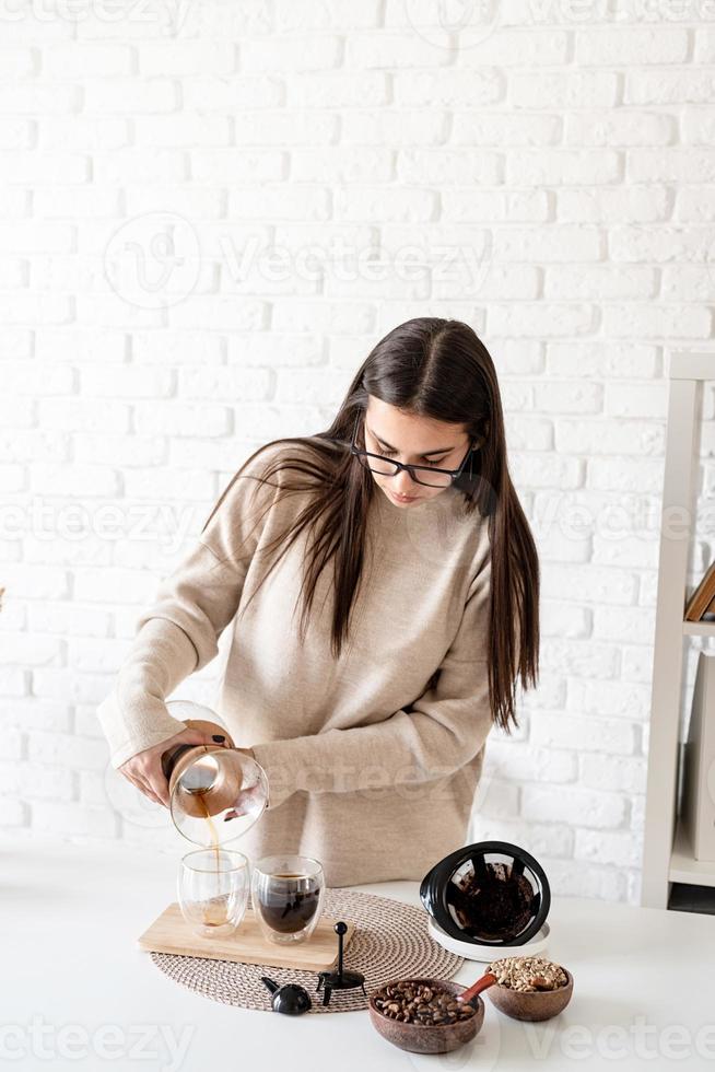 ung kvinna som brygger kaffe i kaffekanna, häller kaffe i glaset foto