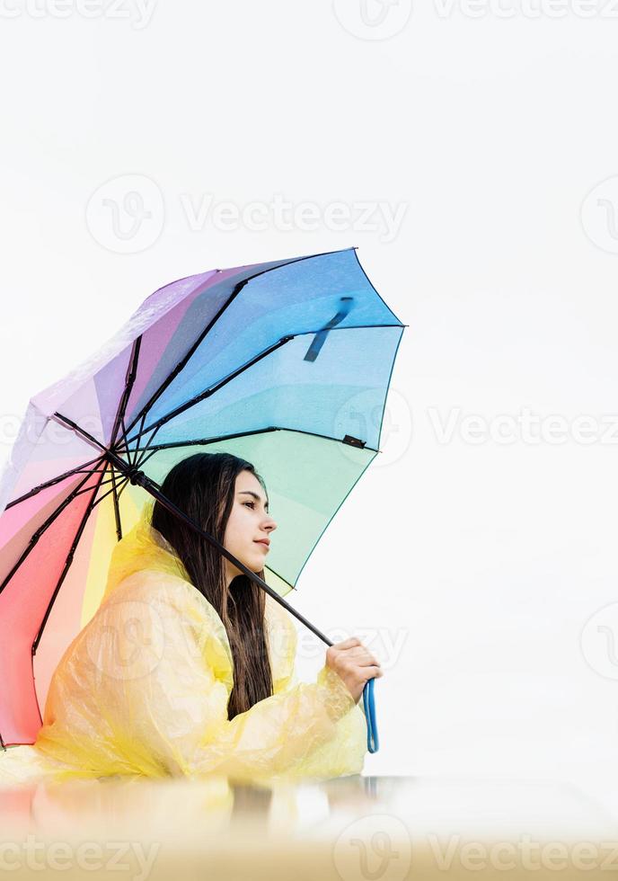 tankeväckande kvinna som står utomhus med ett regnbågsfärgat paraply foto
