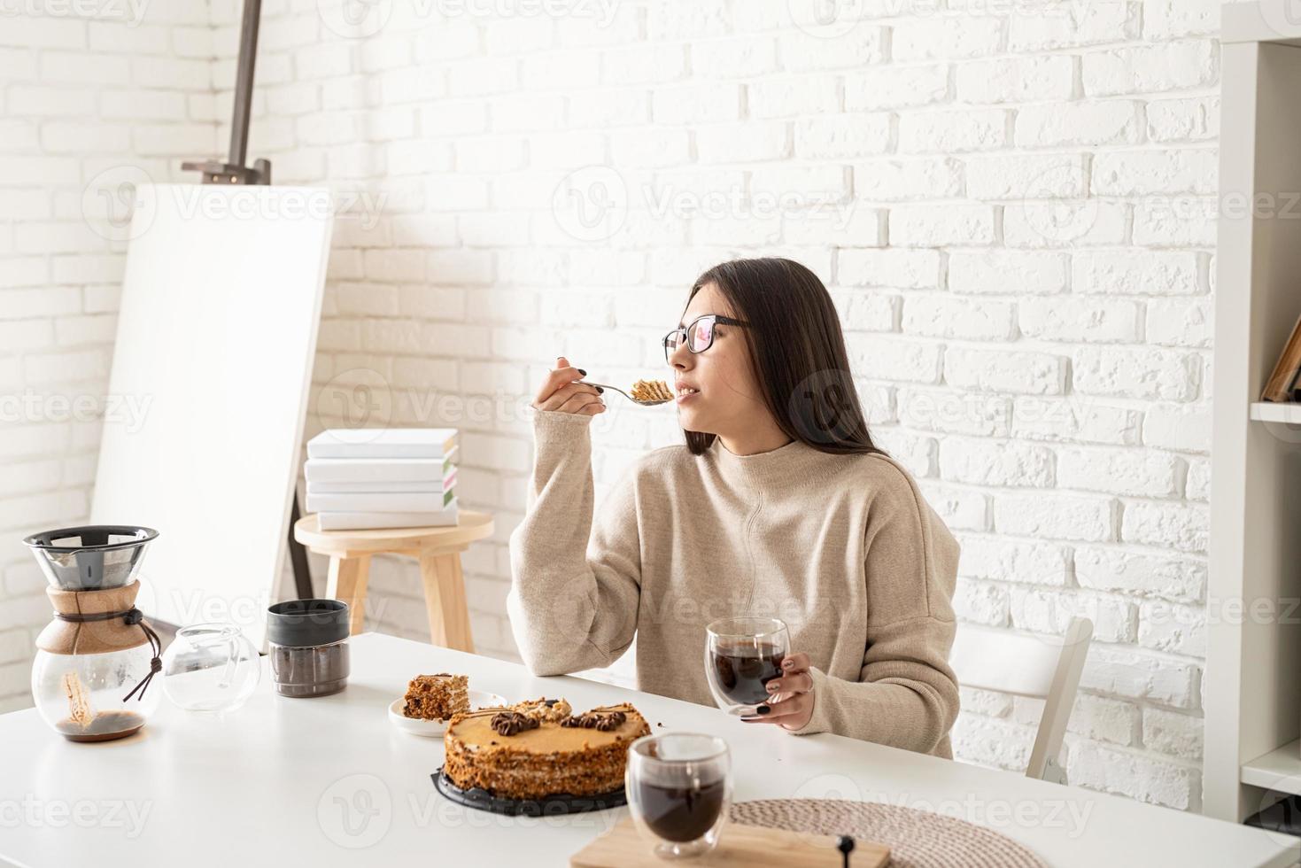 kvinna som sitter vid det vita bordet, äter tårta och dricker kaffe foto