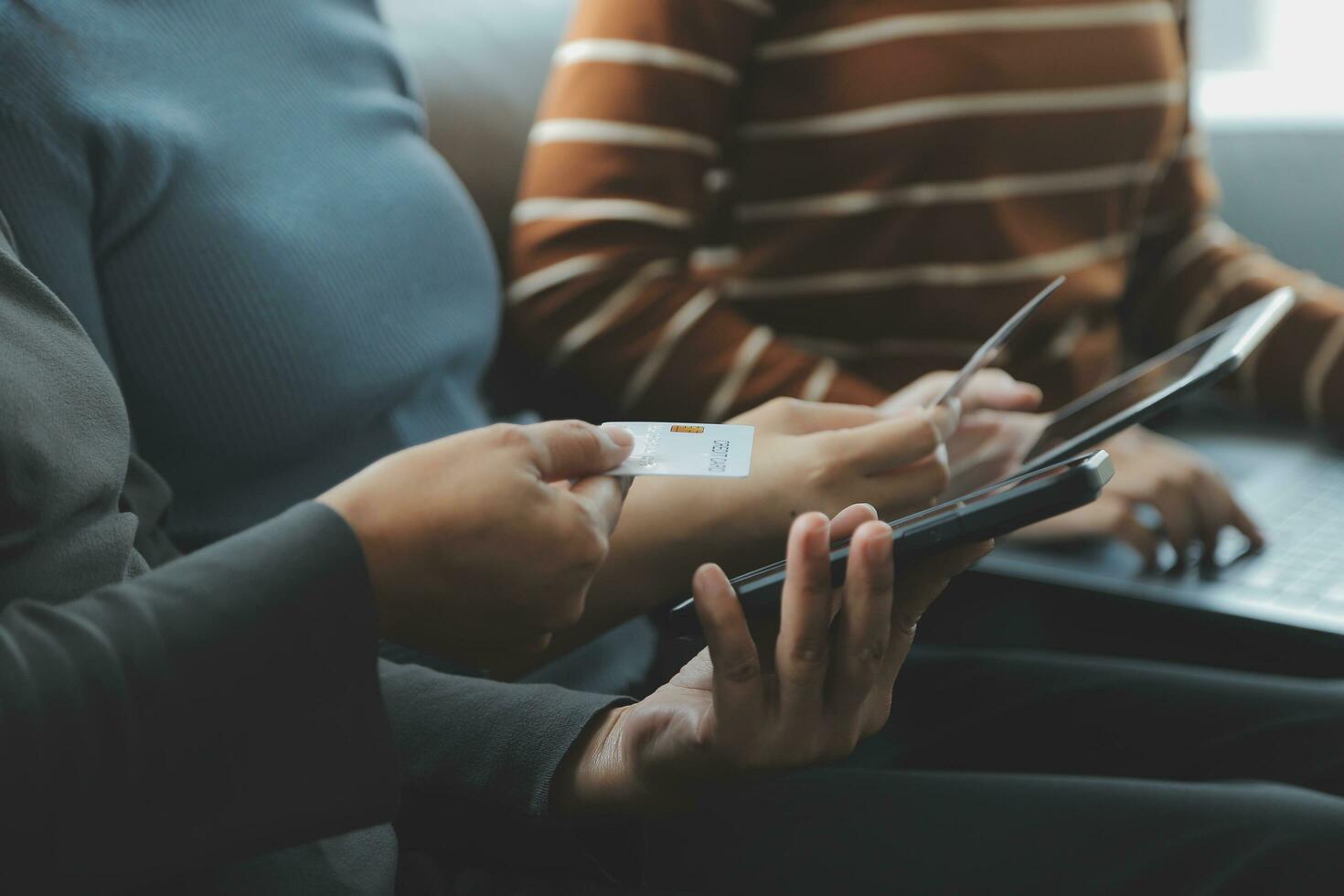 en kreditera kort i de händer av en ung affärskvinna betalar för en företag på en mobil telefon och på en skrivbord med en bärbar dator. foto