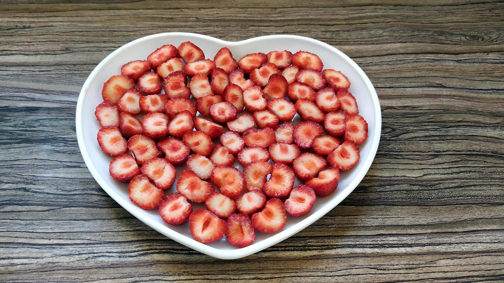 de skivade jordgubbarna finns i en hjärtformad tallrik foto