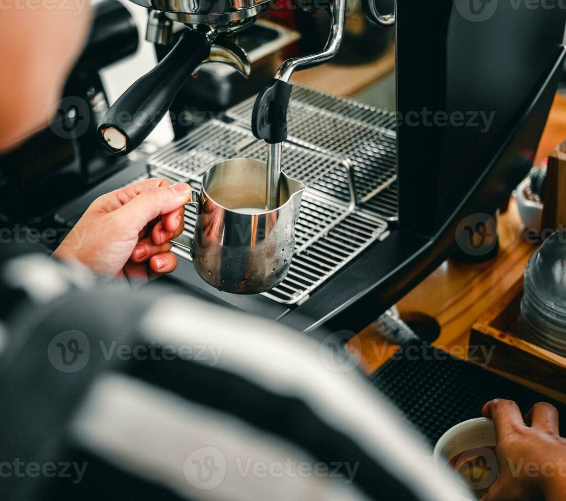 hand av en Barista i de kaffe affär framställning och använder sig av en kaffe maskin till ånga mjölk för en kaffe meny. foto