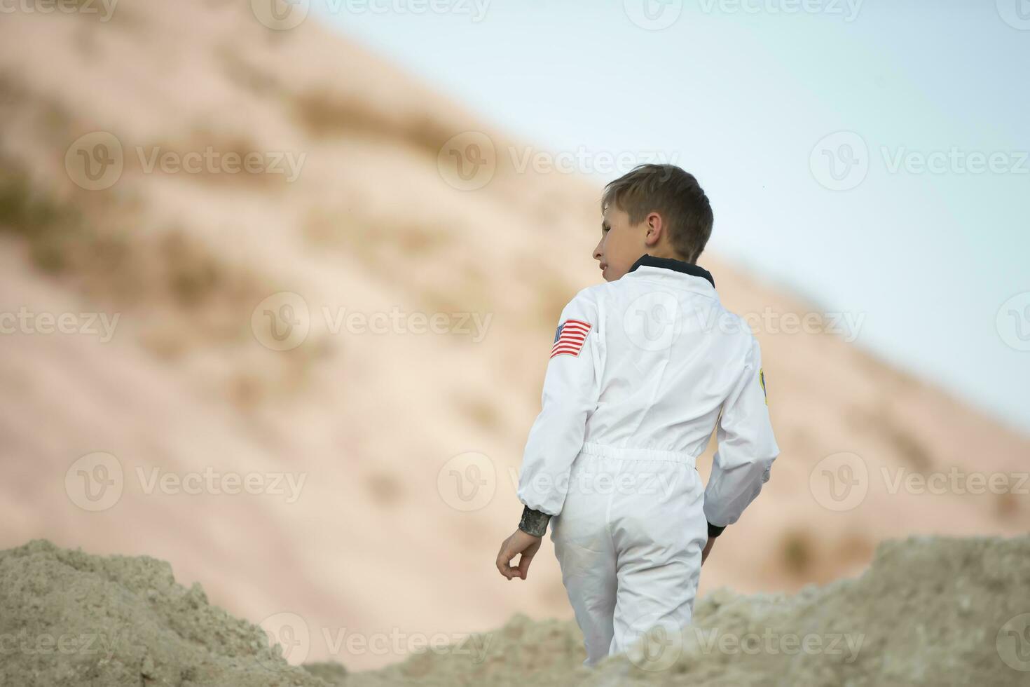 en liten pojke klädd som ett amerikan astronaut promenader genom exotisk bergen av vit sand. foto