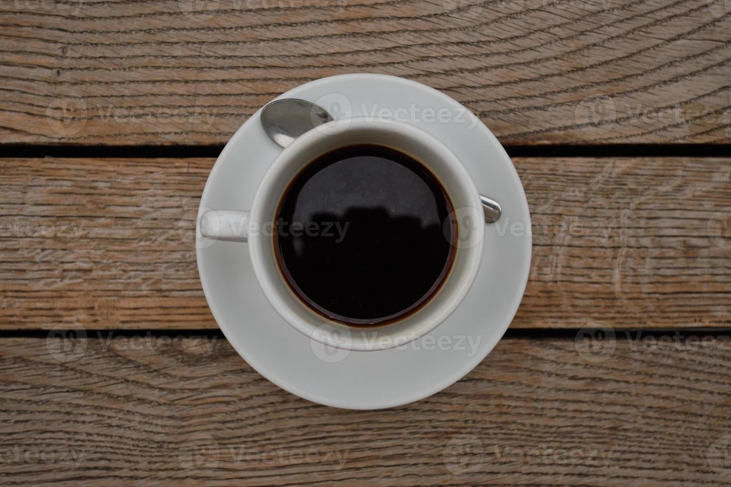 ovanifrån av ett svart kaffe i en kopp på ett fat vid träbordet foto