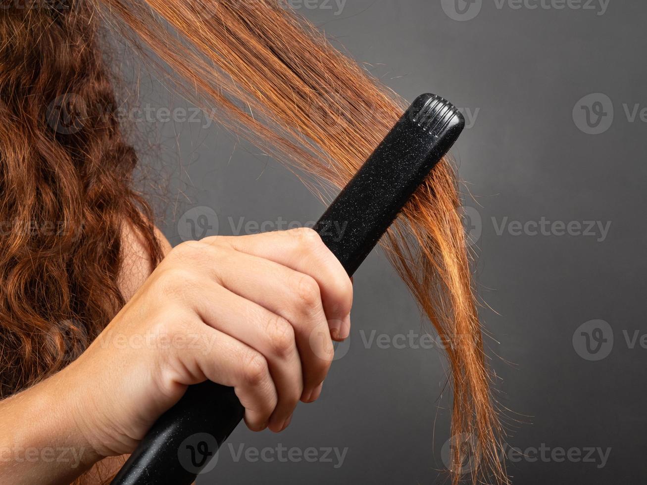 tjejen slätar ut lockigt hår med en plattång, lockjärn. foto