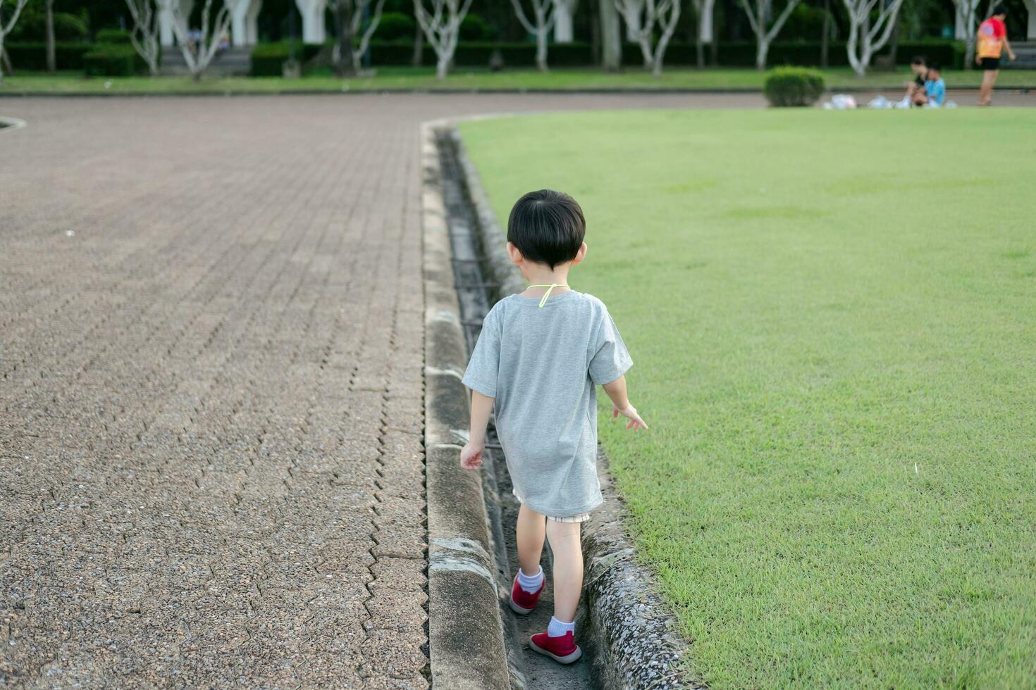 asiatisk pojke spelar, balansering i en dränering dike foto