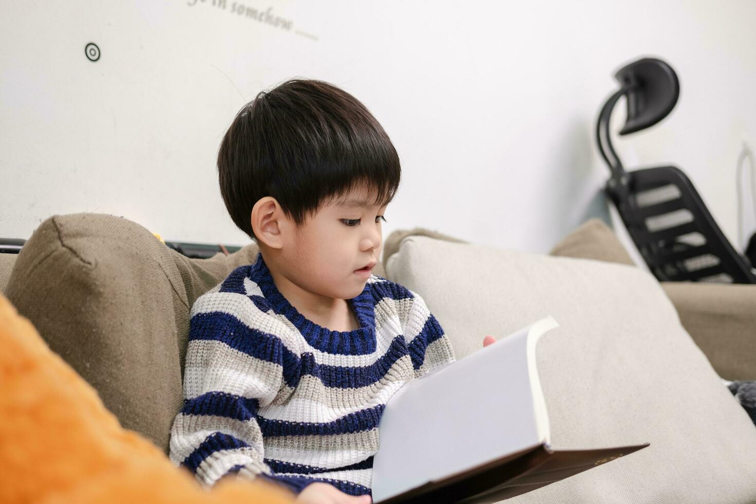 asiatisk pojke läsning en bok på de soffa inlärning utanför de klassrum foto