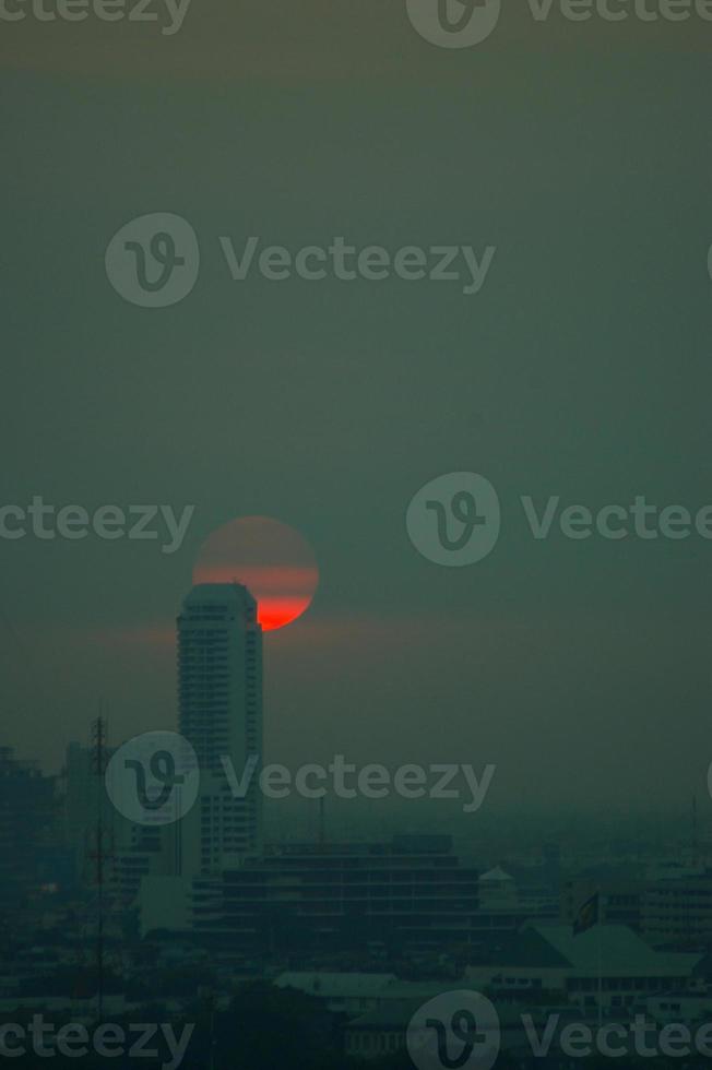 den röda solen på kvällsmolnen och höga byggnader i storstäder foto