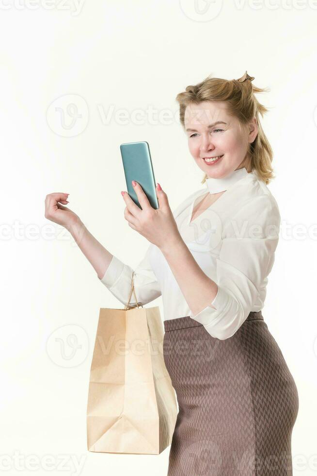 kvinna innehav handla påsar med inköp, leende medan ser på telefon, använder sig av app på smartphone foto
