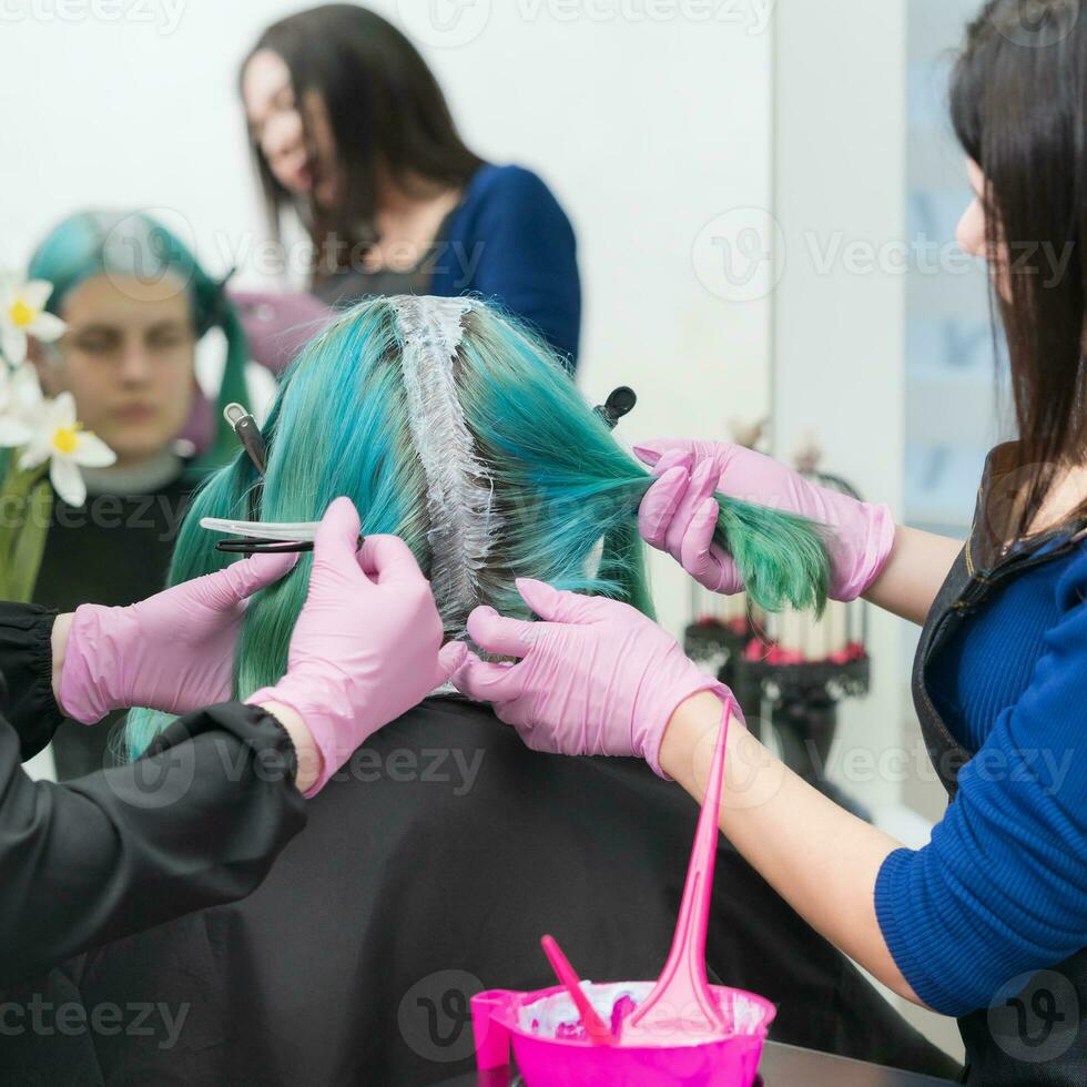 bearbeta av hår färgning i skönhet salong. två frisörer applicering måla till hår under blekning hår rötter foto