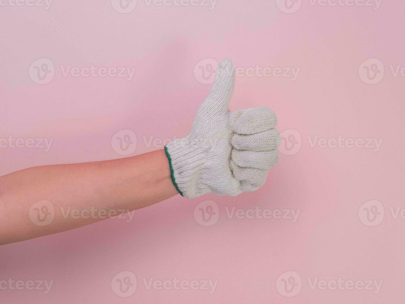 händer i vit stickat handskar isolerat på rosa bakgrund. kvinna hand som visar tumme upp med bomull handskar. foto
