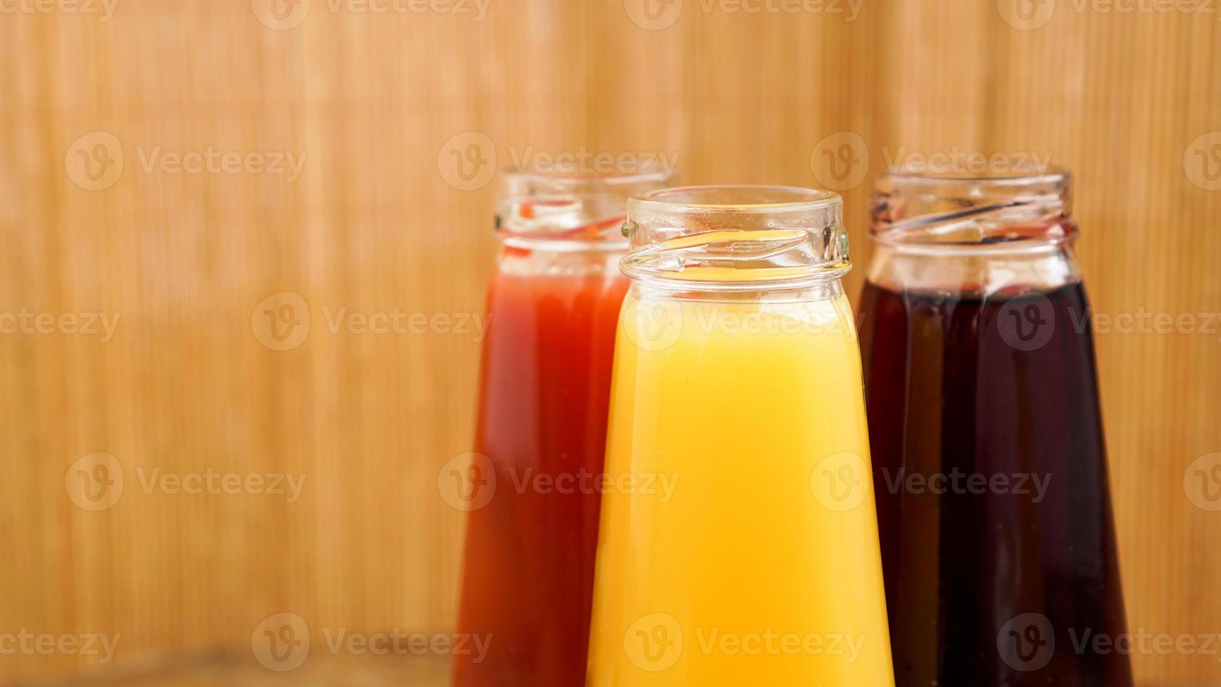 glasflaskor färsk frisk juice på träbakgrund foto