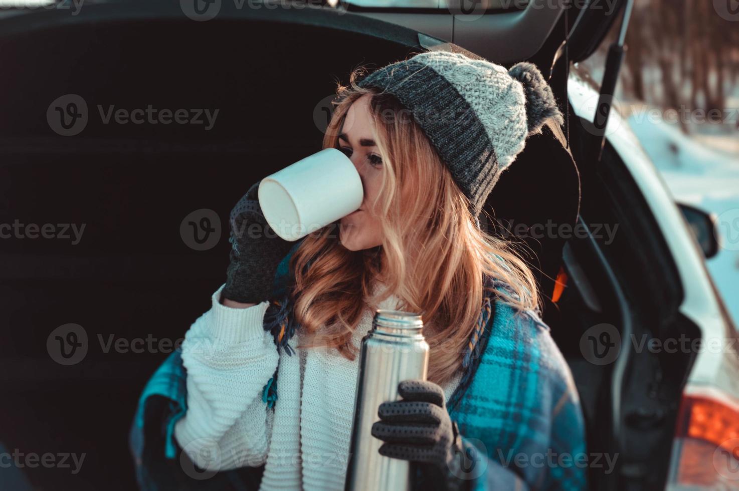 ung kvinna som sitter på bilens bagageutrymme med kaffekopp foto