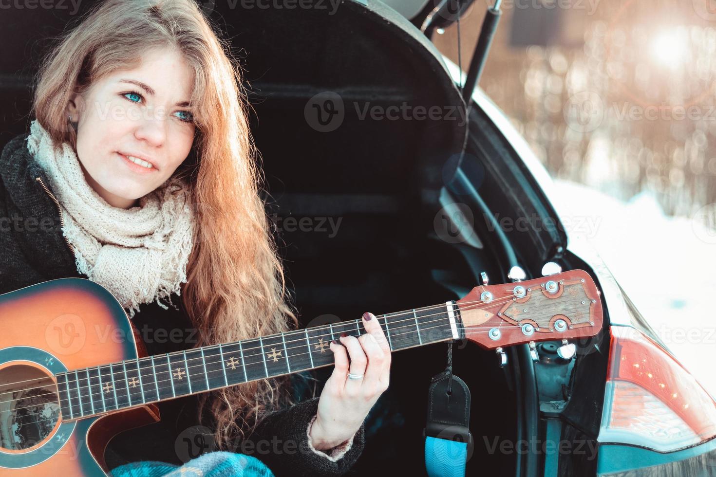 flicka som spelar gitarr som sitter på bilens bagagerum foto