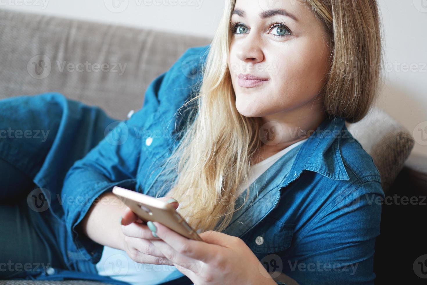 porträtt av drömmande eftertänksam kvinna som ligger på soffan med en smart telefon foto