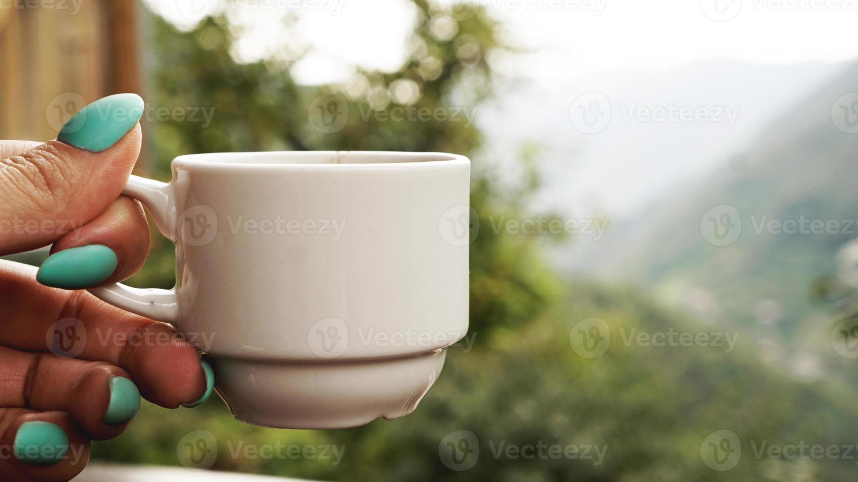 hand vit kopp varmt kaffe. på morgonen, kall utsikt över bergen foto