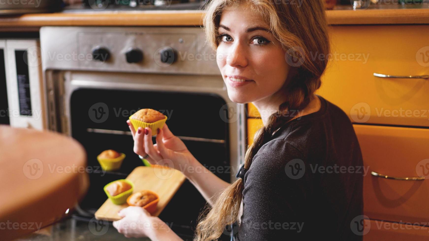 vacker blond kvinna som visar muffins i ett kök foto