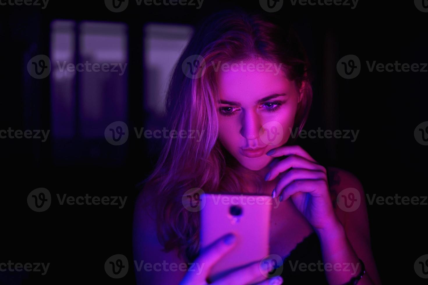 flicka som använder mobiltelefon på natten med neonljus foto