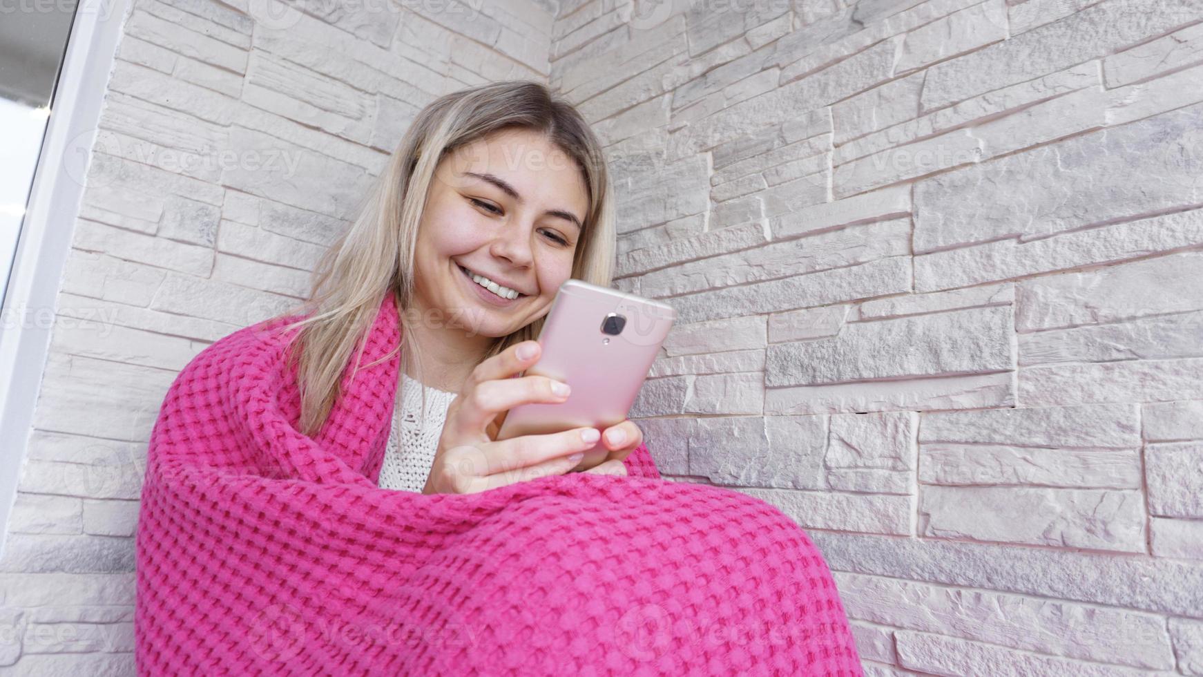 vacker flicka sitter på fönsterbrädan med smartphone i händerna. foto