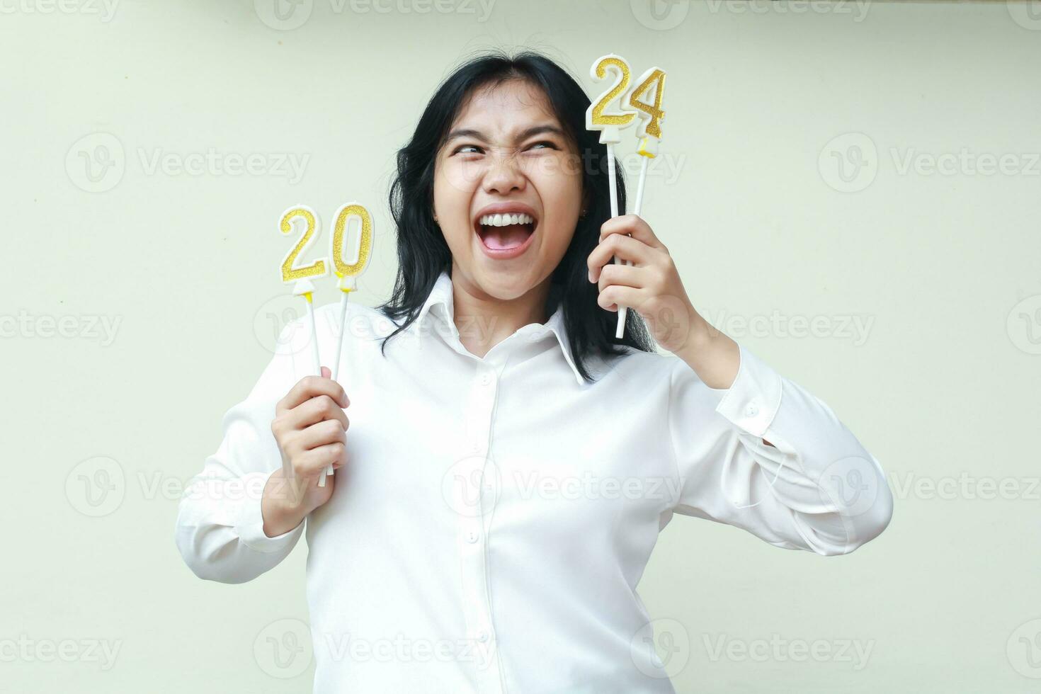 upphetsad asiatisk ung företag kvinna skrikande och ser åt sidan till siffra 24 av 2024 siffra ljus Uppfostrad på hand innehav ha på sig formell vit skjorta, isolerat, ny år eve begrepp foto